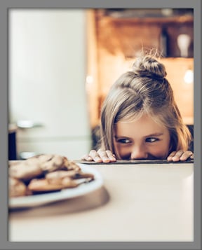 Young girl looking at plate of chocolate chip cookies mischievously