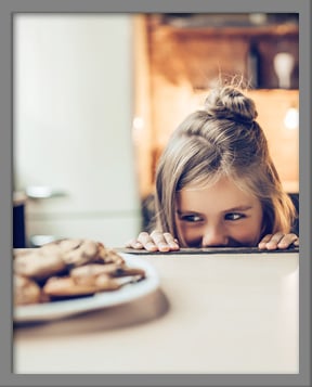 Young girl looking at plate of chocolate chip cookies mischievously Young girl looking at plate of chocolate chip cookies mischievously