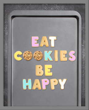 Eat Cookies Be Happy spelled out with cookies cut in the shape of letters on a baking sheet